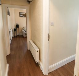 A hallway with wooden flooring and two radiators leading to a living room with a sofa and framed pictures on the wall at Neland View in Windermere