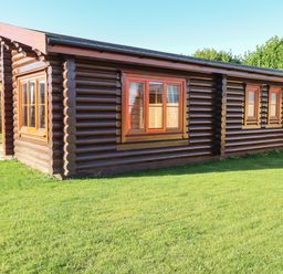 An exterior view of a wooden log cabin with multiple windows and a grass lawn at Elm Lodge Greetham Rutland