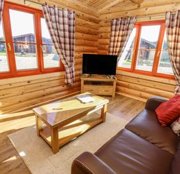 A living room with a brown leather sofa a wooden coffee table a television and plaid curtains at Elm Lodge in Greetham Rutland