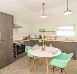 A kitchen with wooden cabinets a round dining table and green chairs at Byghan Thornton in Illogan