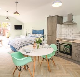 A kitchen and bedroom area with a dining table and two chairs at Byghan Thornton in Illogan