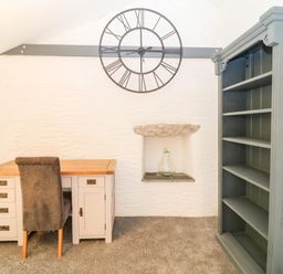 A room with a desk chair bookshelf wall clock and a niche with a glass bottle at Polgear View Polgear Nr Redruth