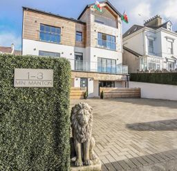 A modern three story building with balconies and a paved parking area with a lion statue and a sign saying 1-3 Min Manton at Bryn Min Manton Apartment in Caernarfon