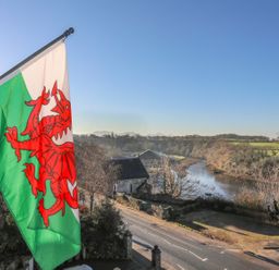 A Welsh flag flying beside a road with a river and trees in the background at Bryn Min Manton Apartment in Caernarfon
