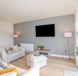 A living room with two sofas a TV on a wall and floor lamps at Bryn Min Manton Apartment in Caernarfon