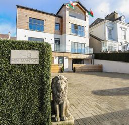A modern residential building with balconies and a driveway with a lion statue at Bryn Min Manton Bach in Caernarfon
