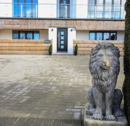 A lion statue on a paved driveway in front of a modern house with a black door at Bryn Min Manton Bach in Caernarfon