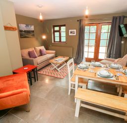 A living room with sofas a dining table set with plates and glasses and wooden benches at Bwthyn Canol in Haverfordwest