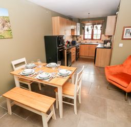 A kitchen and dining area with a wooden dining table set for four a black fridge wooden cabinets and an orange armchair at Bwthyn Canol in Haverfordwest