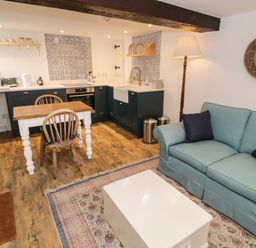 A kitchen and living area with a wooden dining table two chairs a blue sofa a white coffee table and a floor lamp at Gelli Bach at Gelli Las in Llanbedr