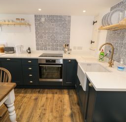 A kitchen with wooden floor blue cabinets oven sink and shelves with dishes at Gelli Bach at Gelli Las in Llanbedr