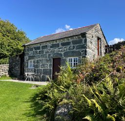A stone cottage with a slate roof surrounded by grass and plants at Gelli Bach at Gelli Las in Llanbedr