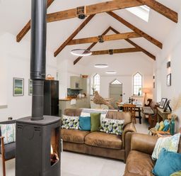 An open-plan living and dining area with leather sofas a wood-burning stove wooden ceiling beams and a kitchen at Ysgoldy Brynwyre in Llanrhystud