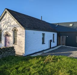 A building with white stone walls and purple door next to a modern black metal extension surrounded by grass at Ysgoldy Brynwyre in Llanrhystud