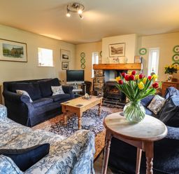A living room with sofas a wooden coffee table a fireplace and flowers on a small table at Tyddyn Bach in Newport Pembrokeshire