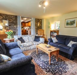 A sitting room with sofas a wooden coffee table a patterned rug a vase with flowers and a bookshelf at Tyddyn Bach Newport Pembrokeshire