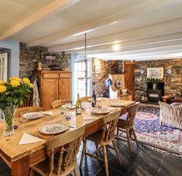 A dining area with a wooden table set with plates and glasses and a seating area with wicker and wooden furniture at Tyddyn Bach in Newport Pembrokeshire