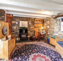 A living room with stone walls wooden furniture a fireplace and a patterned rug at Tyddyn Bach in Newport Pembrokeshire