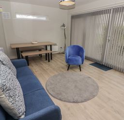 A living room with a blue sofa and chair a wooden dining table with benches and vertical blinds at 21 Coedrath Park in Saundersfoot