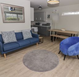 A living room with a blue sofa a blue armchair a round gray rug a wooden dining table with benches and a wall mirror at 21 Coedrath Park Saundersfoot
