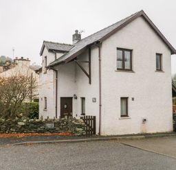 A white two-story house with a stone wall and tree on the side with a sign saying Abbots Vue at Friars Fold in Newby Bridge