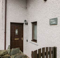An exterior view of a house entrance with a brown door a window a stone wall a wooden gate and a sign that reads Friars Fold in Newby Bridge