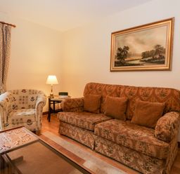 A living room with a patterned sofa a floral armchair a lamp on a side table and a landscape painting at Friars Fold in Newby Bridge
