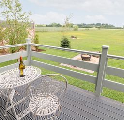 A patio with a white metal table and two chairs with a bottle on the table and a grassy field with a fire pit in the background at Buttercup Lodge in Misterton