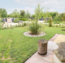 A garden with a circular plant bed and a wooden stool next to a stone bench at Buttercup Lodge in Misterton
