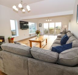 A living room with a large sofa a wooden coffee table a fireplace and a wall-mounted television at Yr Hen Feudy in Moelfre