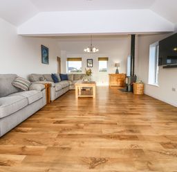 A living room with gray sofas a coffee table a wood stove and a wall-mounted television at Yr Hen Feudy in Moelfre