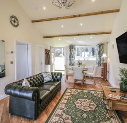 A living room with a green leather sofa wooden dining table with chairs a wall clock and a mounted television at FAIRFIELD in Clee Hill