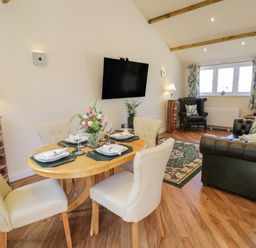 A dining area with a round wooden table set for four and a living room with green leather sofas and a patterned rug at FAIRFIELD in Clee Hill