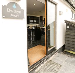An open doorway showing a kitchen with black cabinets and bar stools at Bwthyn Awel Church Bay near Cemaes Bay