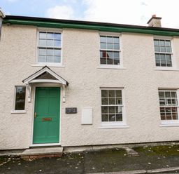 The exterior of a white textured house with a green door and multiple windows at Bridgend Cottages in Howey near Llandrindod Wells