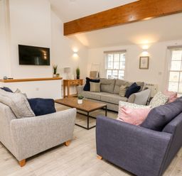 A living room with three sofas a wooden coffee table a wall-mounted TV and wooden beams at Bridgend Cottages in Howey near Llandrindod Wells