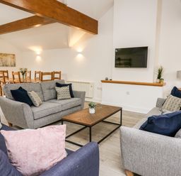 A living room with two gray sofas a blue armchair a wooden coffee table and a mounted TV at Bridgend Cottages in Howey near Llandrindod Wells