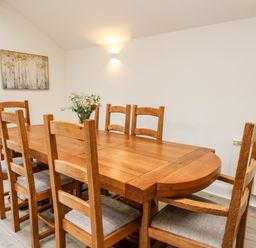 A dining room with a wooden table and eight chairs with a flower vase on the table at Bridgend Cottages in Howey near Llandrindod Wells
