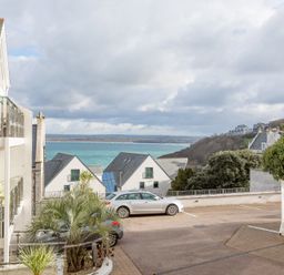 A parking area with two cars near white houses and a view of the sea at The Waves in St Ives