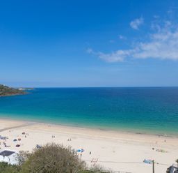 A sandy beach with people and umbrellas by a blue ocean under a clear sky at Turquarze in Carbis Bay