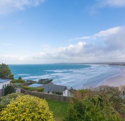 A coastal view with houses, trees, and waves on the beach at Whitsunday House in Carbis Bay