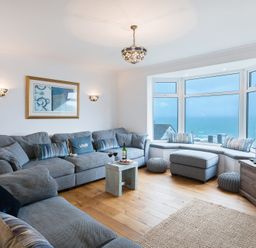 A living room with grey sofas a small wooden table large windows with a sea view and a wooden TV stand at Whitsunday House in Carbis Bay