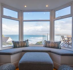 A seating area with cushions by a large bay window overlooking the sea at Whitsunday House in Carbis Bay