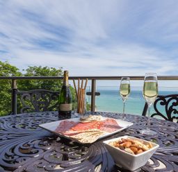 A table on a balcony with wine glasses bottle charcuterie and nuts overlooking the sea at Abalone in St Ives
