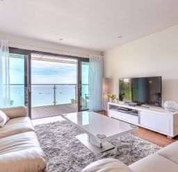 A living room with leather sofas a white coffee table a TV on a stand and a view of the sea at Abalone in St Ives