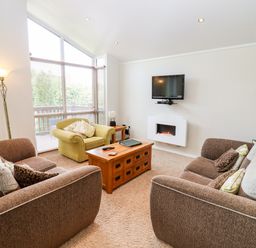 A living room with two brown sofas a green armchair a wooden coffee table a wall-mounted television and an electric fireplace at Oak Lodge in Glasshouse