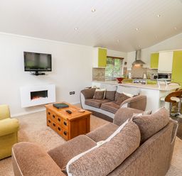 A living room with brown and green sofas a wooden coffee table a wall mounted TV and a kitchen with green cabinets at Oak Lodge in Glasshouse