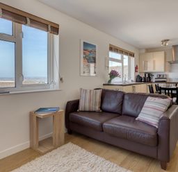 A living room with a brown leather sofa and striped cushions next to a wooden side table and window with a view at Atlantic Blue in Carbis Bay