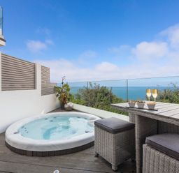 A balcony with a hot tub a wicker table and stools and ocean view at Atlantic Watch 8 in Carbis Bay