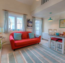 A living room with a red sofa and blue cushions next to a dining table with chairs and a map on the wall at Brinyloft in Carbis Bay